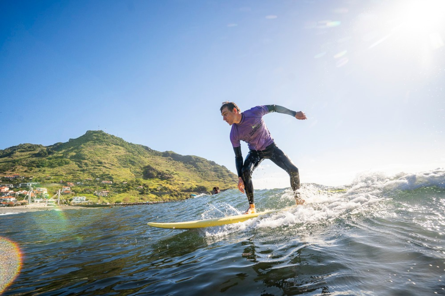 Male surfer riding a wave in a sunny day while doing a beginner surf lesson in machico