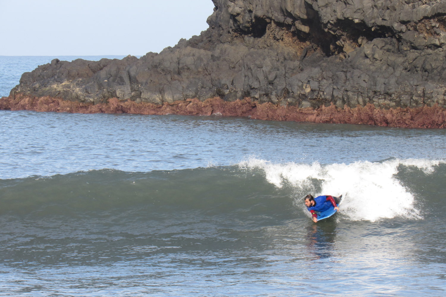 Male bodyboarder riding a wave while doing his group bodyboard lesson in madeira in a volcanic beach