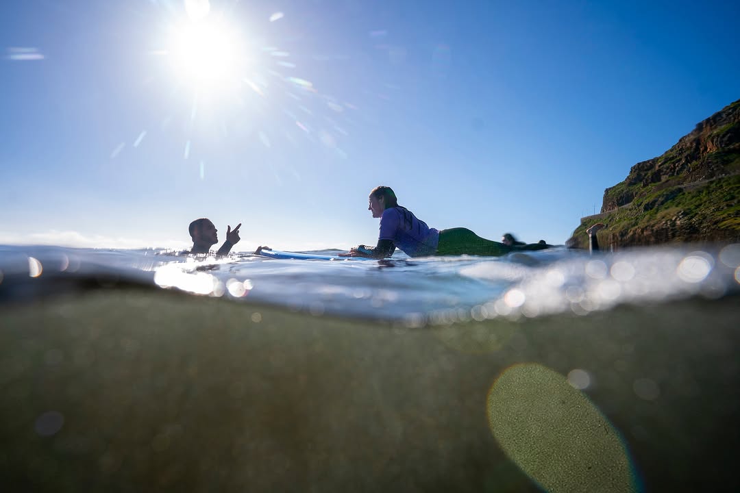 Instructor giving advice to the surfer that's laying in the surfboard while doing a private surf lesson in madeira