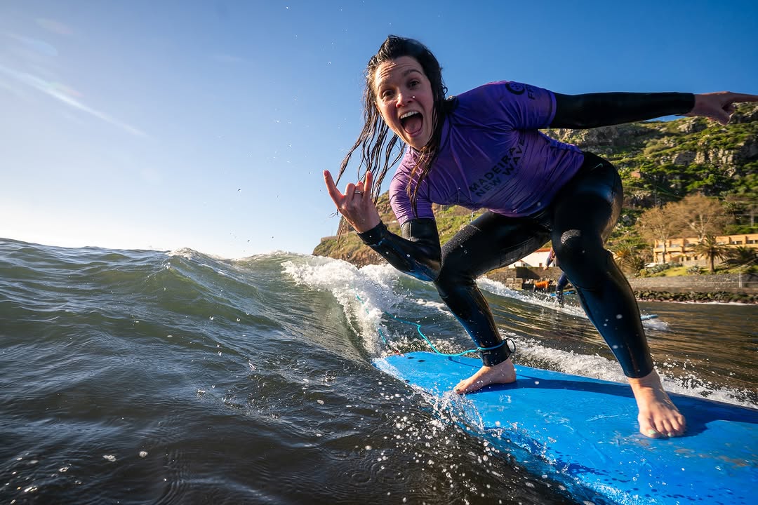 Happy woman surfer riding a wave during her group surf lessons in madeira