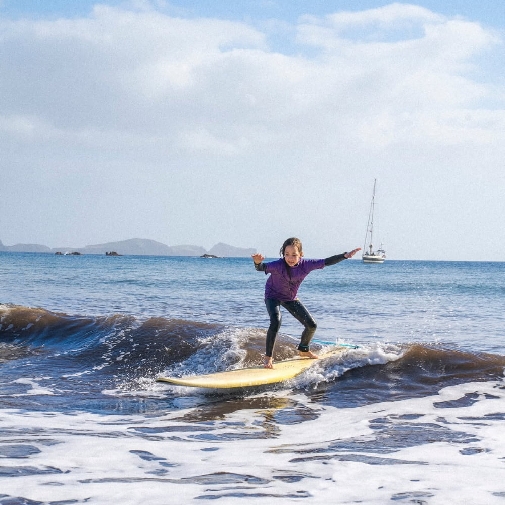 Young kid riding a wave while doing a kids surf lesson in madeira