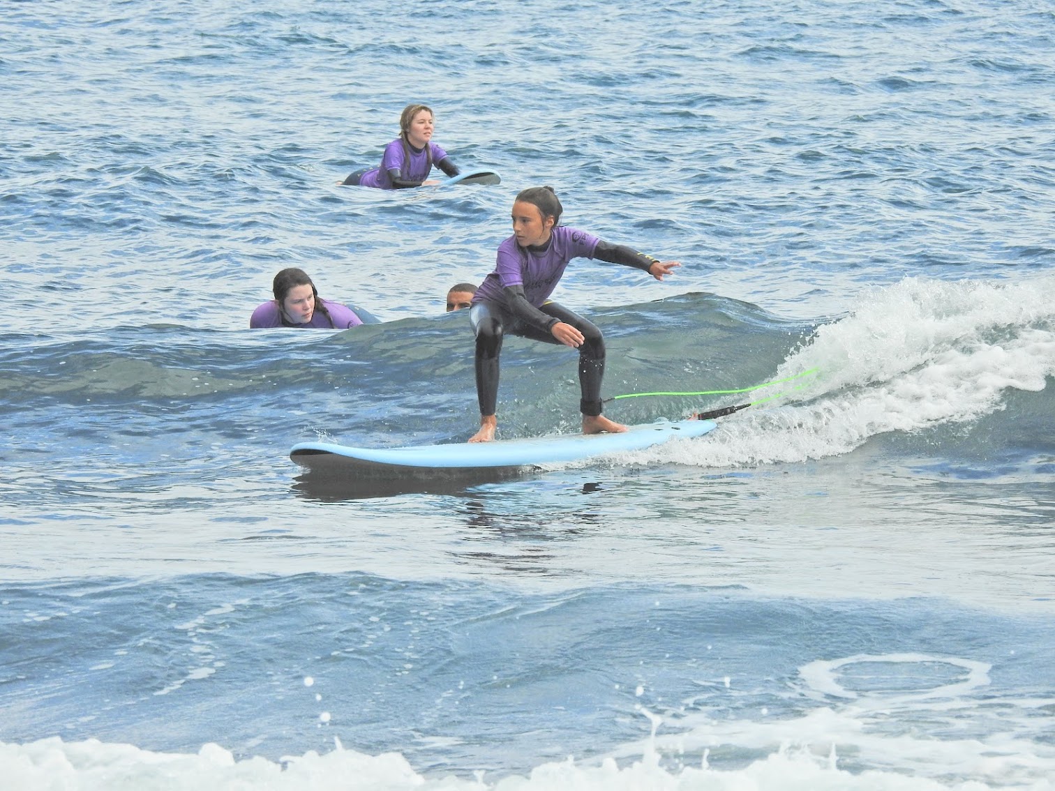 Young kid riding a wave while her group watches her during her kids surf lesson in madeira