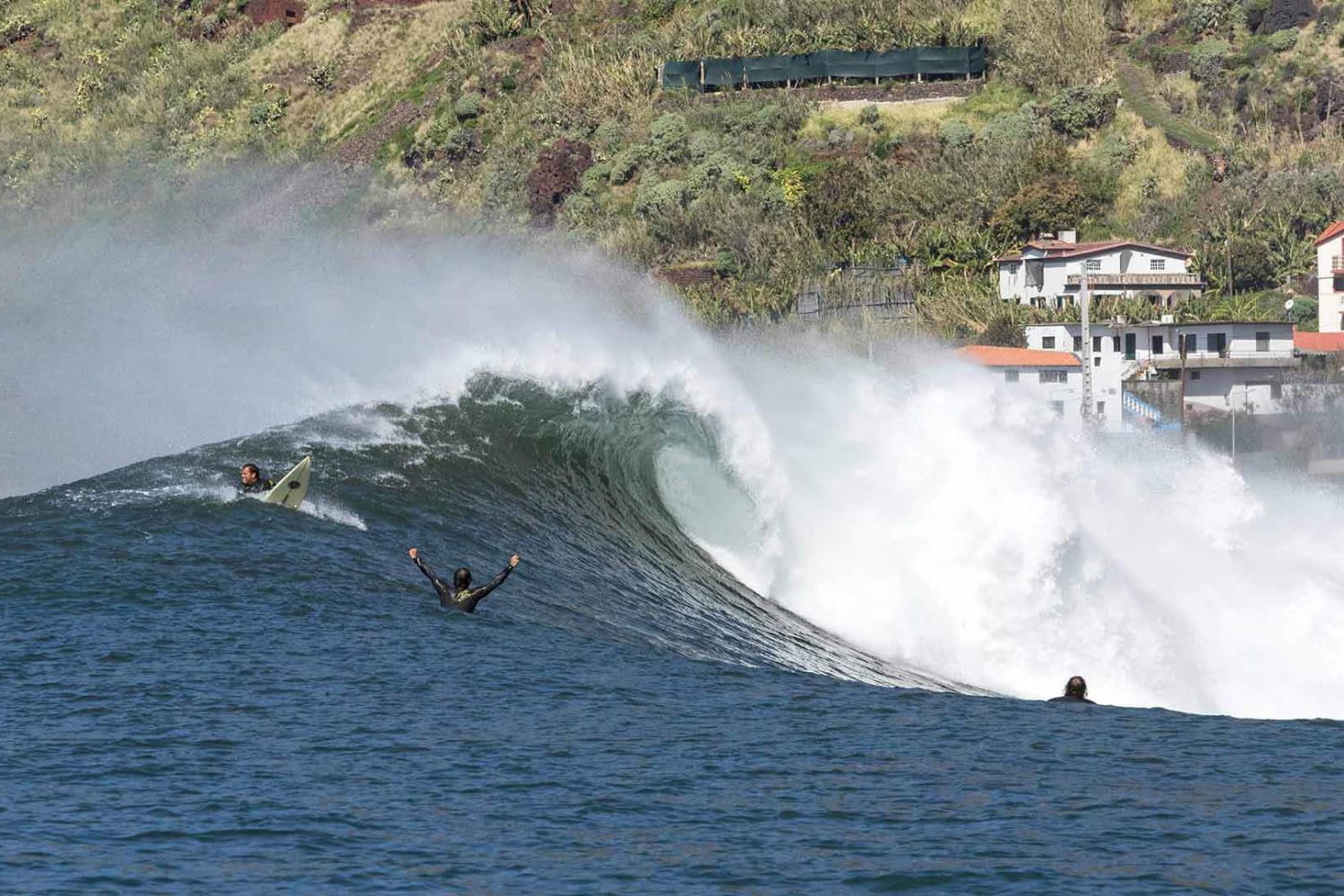 Big wave with surfers riding it in Paul do mar with the help of a surf guide